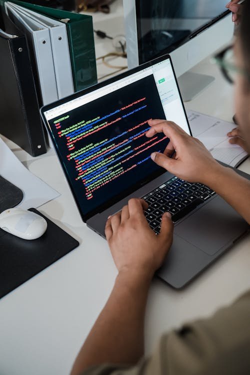 Free Close-up of a programmer pointing at a colorful code script on a laptop in an office setting. Stock Photo